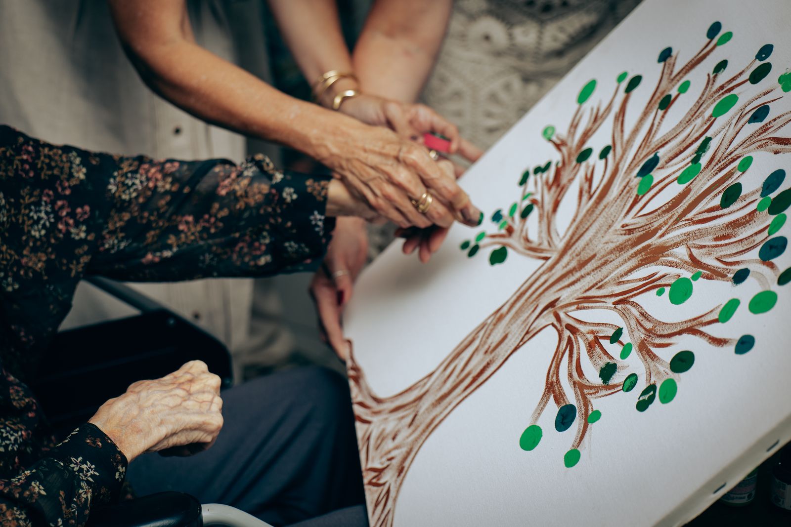 A senior's hand painting part of a collaborative tree artwork