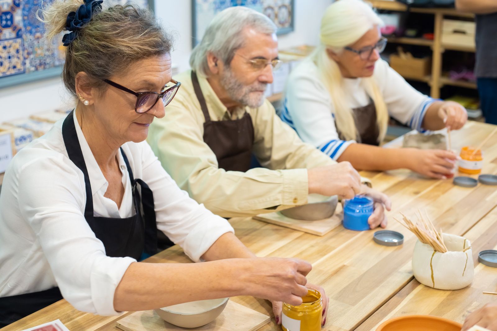 A group of senior adults enjoying a pottery painting workshop together at a shared table