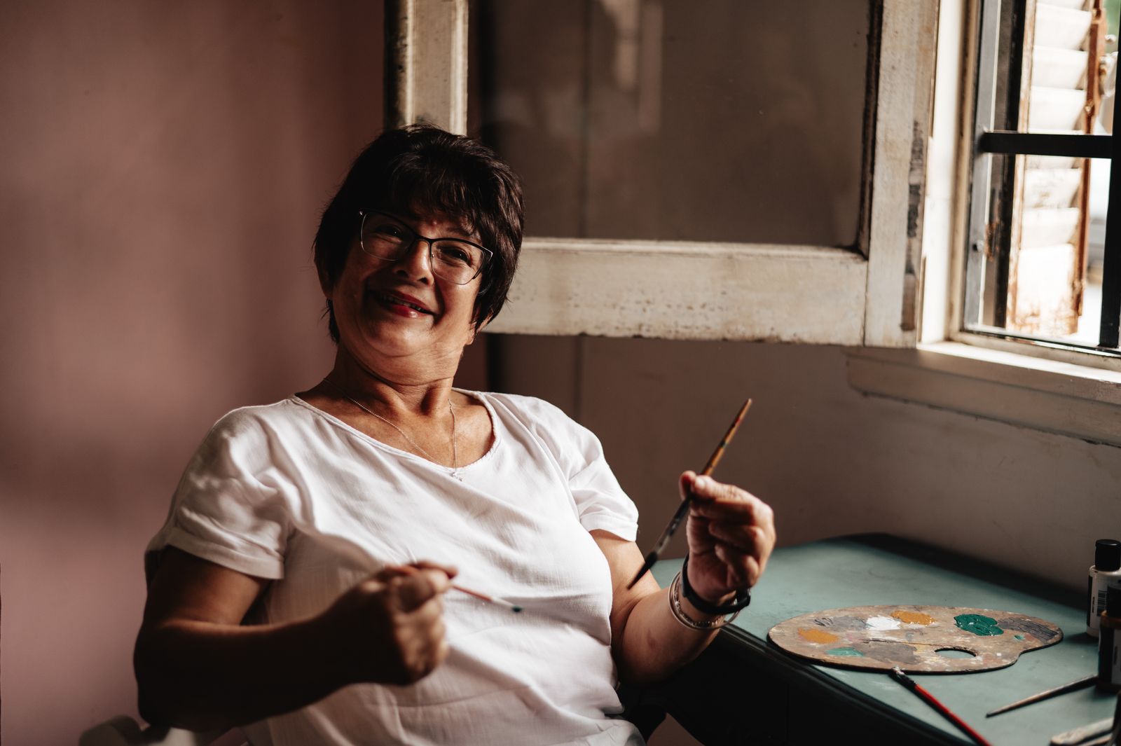 A senior woman artist smiling in a cozy, light-filled studio